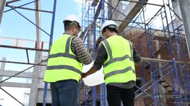 İki inşaat işçisi şantiyede duruyor ve çalışma planlarını tartışıyorlar.