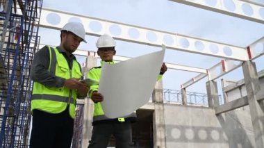İki inşaat işçisi şantiyede duruyor ve çalışma planlarını tartışıyorlar.