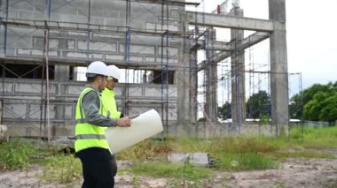 İnşaat alanında iki inşaat işçisi çalışma planlarını tartışıyor.