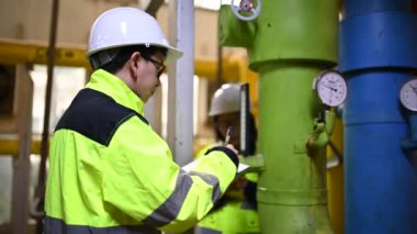 Fabrikadaki petrol ve gaz boru hatlarını kontrol eden iki mühendis.