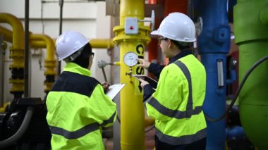 Fabrikadaki petrol ve gaz boru hatlarını kontrol eden iki mühendis.