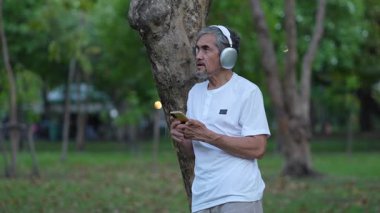 Ağaca yaslanırken akıllı telefon kullanan kulaklıklı son sınıf öğrencisi.