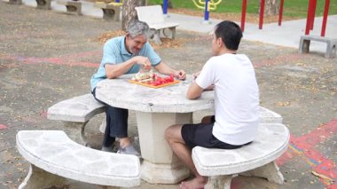 İki Asyalı parkta satranç oynuyor.