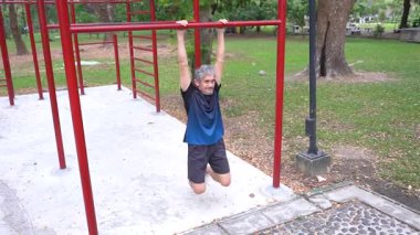 Kıdemli Asyalı adam parkta yatay barda egzersiz yapıyor.