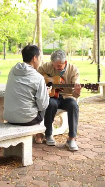 Gri kapüşonlu adamla parkta gitar çalan son sınıf öğrencisi.