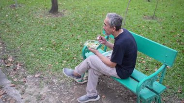 Son sınıf öğrencisi parkta bankta otururken sağlıklı salata yiyor.