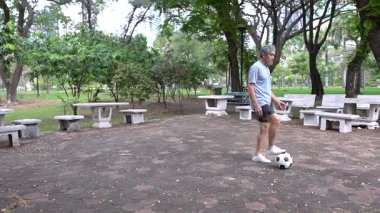 Yetişkin Asyalı son sınıf öğrencisi parkta futbol topuyla oynuyor..