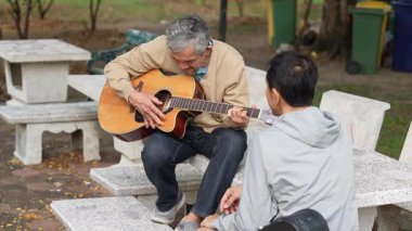 Gri kapüşonlu bir adamla parkta gitar çalıyordu.
