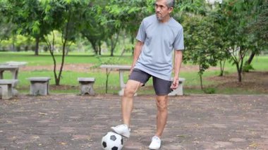 Yetişkin Asyalı son sınıf öğrencisi parkta futbol topuyla oynuyor..