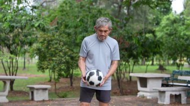 Yetişkin Asyalı son sınıf öğrencisi parkta futbol topuyla oynuyor..
