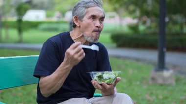 Son sınıf öğrencisi parkta bankta otururken sağlıklı salata yiyor.