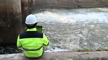 Çevre mühendisi su kalitesini kontrol ediyor ve dışarıda dizüstü bilgisayar kullanıyor.