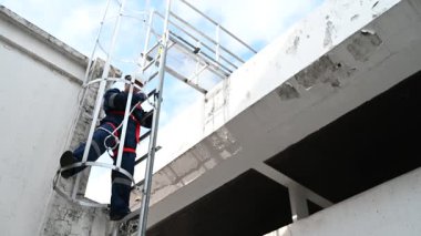 Miğferli ve koruyucu kıyafetli bir işçi metal merdivene tırmanıyor.