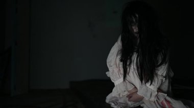 Yüzünde hayalet resmi olan korkunç kadın karanlıkta poz veriyor.