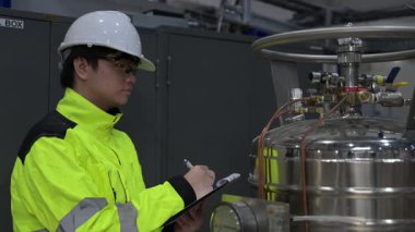 Operasyon salonunda çalışan Asyalı mühendis, Taylandlı adam kask takıyor, özen ve sabırla çalışıyor, hidrojen tankının kapakçık düzenleyicisini kontrol ediyor..