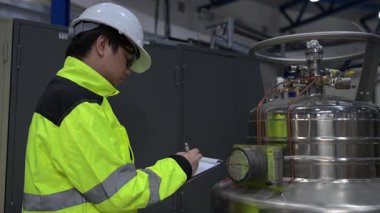 Operasyon salonunda çalışan Asyalı mühendis, Taylandlı adam kask takıyor, özen ve sabırla çalışıyor, hidrojen tankının kapakçık düzenleyicisini kontrol ediyor..