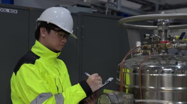 Operasyon salonunda çalışan Asyalı mühendis, Taylandlı adam kask takıyor, özen ve sabırla çalışıyor, hidrojen tankının kapakçık düzenleyicisini kontrol ediyor..