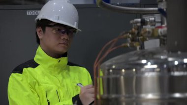 Operasyon salonunda çalışan Asyalı mühendis, Taylandlı adam kask takıyor, özen ve sabırla çalışıyor, hidrojen tankının kapakçık düzenleyicisini kontrol ediyor..