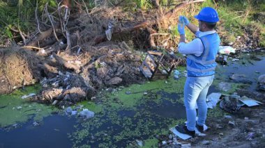 Adam çöplerle dolu nehirde su kalitesini kontrol ediyor. Kirlilik sorunu kavramı 