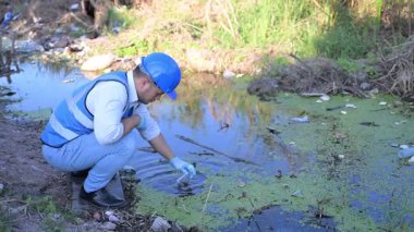 Kirli bir nehirde su kalitesini ölçen adam. 