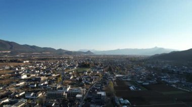 Baisha Kadim Kasabası 'nın üzerinde süzülen bir video. Çatıları vadi boyunca uzanan geleneksel evler. Dağlar ufku kucaklıyor 