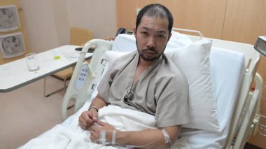 Doktor hasta Asyalı bir adamın hastane yatağında sıcaklığını kontrol ediyor. 