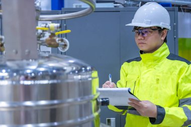 Operasyon salonunda çalışan miğferli Asyalı mühendis. Hidrojen tankındaki valf regülatörünü kontrol ediyor..