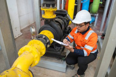 Kazan dairesinde çalışan gözlüklü Asyalı mühendis ısıtma sistemi ekipmanlarının teknik verilerini kontrol ediyor.