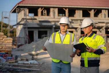 Büyük bir inşaat projesinin şantiyesinde çalışan iki Asyalı mühendis inşaat sahasında fazla mesai, inşaat alanında mühendislik diski.