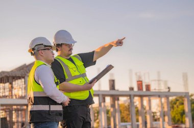 Büyük bir inşaat projesinde çalışan iki Asyalı mühendis. İnşaat alanında fazla mesai.