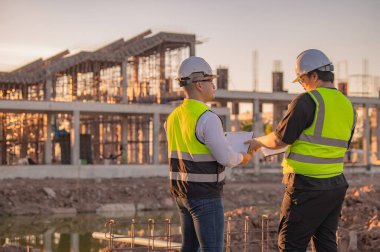 Büyük bir inşaat projesinde çalışan iki Asyalı mühendis. İnşaat alanında fazla mesai.