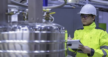 Operasyon salonunda çalışan miğferli Asyalı mühendis. Hidrojen tankındaki valf regülatörünü kontrol ediyor..