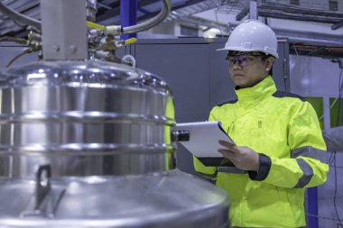 Operasyon salonunda çalışan miğferli Asyalı mühendis. Hidrojen tankındaki valf regülatörünü kontrol ediyor..