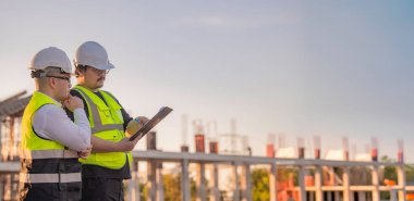 Büyük bir inşaat projesinde çalışan iki Asyalı mühendis. İnşaat alanında fazla mesai.