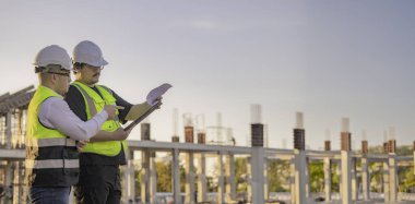 Büyük bir inşaat projesinde çalışan iki Asyalı mühendis. İnşaat alanında fazla mesai.