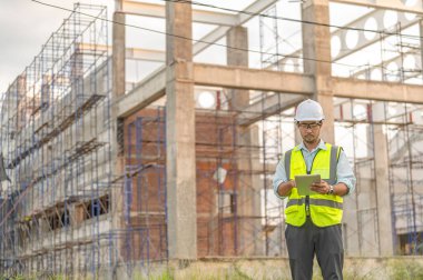 Büyük bir inşaat projesinin şantiyesinde çalışan Asyalı mühendis. İnşaat alanında fazla mesai.