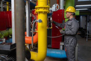 Kazan dairesinde çalışan gözlüklü Asyalı mühendis ısıtma sistemi ekipmanlarının teknik verilerini kontrol ediyor. 