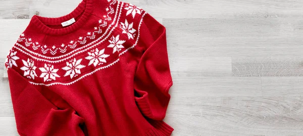 Flat lay red knitted christmas sweater on wooden background. Knitted winter pullover top view empty copy space. Holiday decoration. Seasonal clothes.