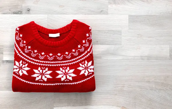 Flat lay folded red knitted christmas sweater on wooden background. Knitted winter pullover top view empty copy space. Holiday decoration. Seasonal clothes.