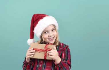 Noel Baba şapkalı çocuk mavi arka planda hediye kutusunu tutuyor. Noel kostümü giymiş, elinde hediyeyle beyaz çocuk portresi. Mutlu küçük bebek yeni yıl konsepti.