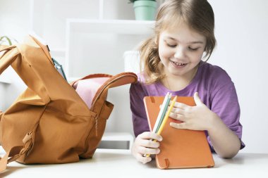 Kız çocuğu okula hazırlanıyor. Okula, erzaklara. Kırmızı çantalı çocuk. Öğrenci. Anaokulu öğrencisi..