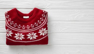 Düz, beyaz ahşap arka planda katlanmış kırmızı örülü Noel süveteri. Örülmüş kış kazağı boş fotokopi alanı. Tatil dekorasyonu. Mevsimlik kıyafetler.