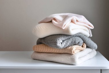 Masanın üzerinde yumuşak, sıcak örülmüş giysiler, yünlü çamaşırlar, kışlık giysiler, bir yığın örgü..