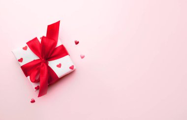 Boş pembe arka planda kırmızı bağlı yemin kalbi olan hediye kutusu. Sevgililer günü kartı. Romantik tatil arkaplanı.