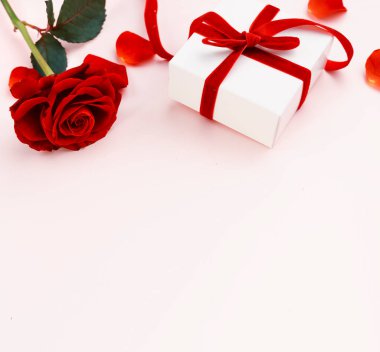 Kırmızı gül ve hediye kutusu üst görünümü yumuşak pembe boş arkaplanda. Sevgililer günü kartı, romantik tatil çerçevesi. Doğum günü hediyesi. Kadınlar günü sınırı..