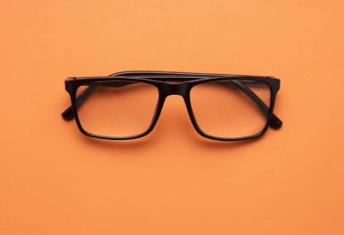Gözlük düzlüğü turuncu arka plana yakın çekim. Görme objesi. Siyah gözlük üst görüş, hiç kimse. Optik kavram..
