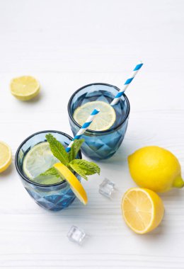 Limon ve limonla süslenmiş beyaz ahşap masa üzerinde bir bardak limonlu buzlu su. Taze narenciye suyu, ferahlatıcı içecek, boş fotokopi alanı..