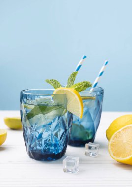 Limon ve limonla süslenmiş beyaz ahşap masa üzerinde bir bardak limonlu buzlu su. Taze narenciye suyu, ferahlatıcı içecek, boş fotokopi alanı..