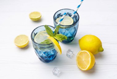 Limon ve limonla süslenmiş beyaz ahşap masa üzerinde bir bardak limonlu buzlu su. Taze narenciye suyu, ferahlatıcı içecek, limonata..