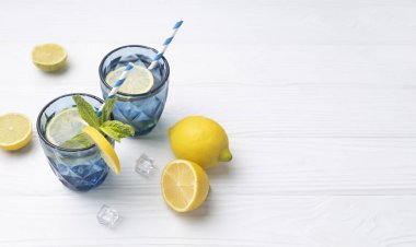 Limonata, mavi bardakta limon suyu, boş beyaz ahşap arka planda sarı limonlarla süslenmiş. Yaz içeceği, sağlıklı detoks içeceği. Vitamin içeceği..